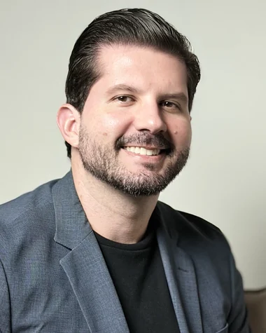 Dr. Joaquim Menezes sorrindo, de blazer cinza, sobre fundo claro